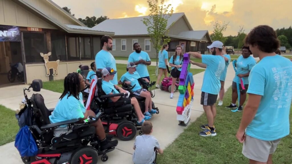 Photo of campers in wheelchairs and volunteers at Camp Kamassa playing balancing game on the green.
