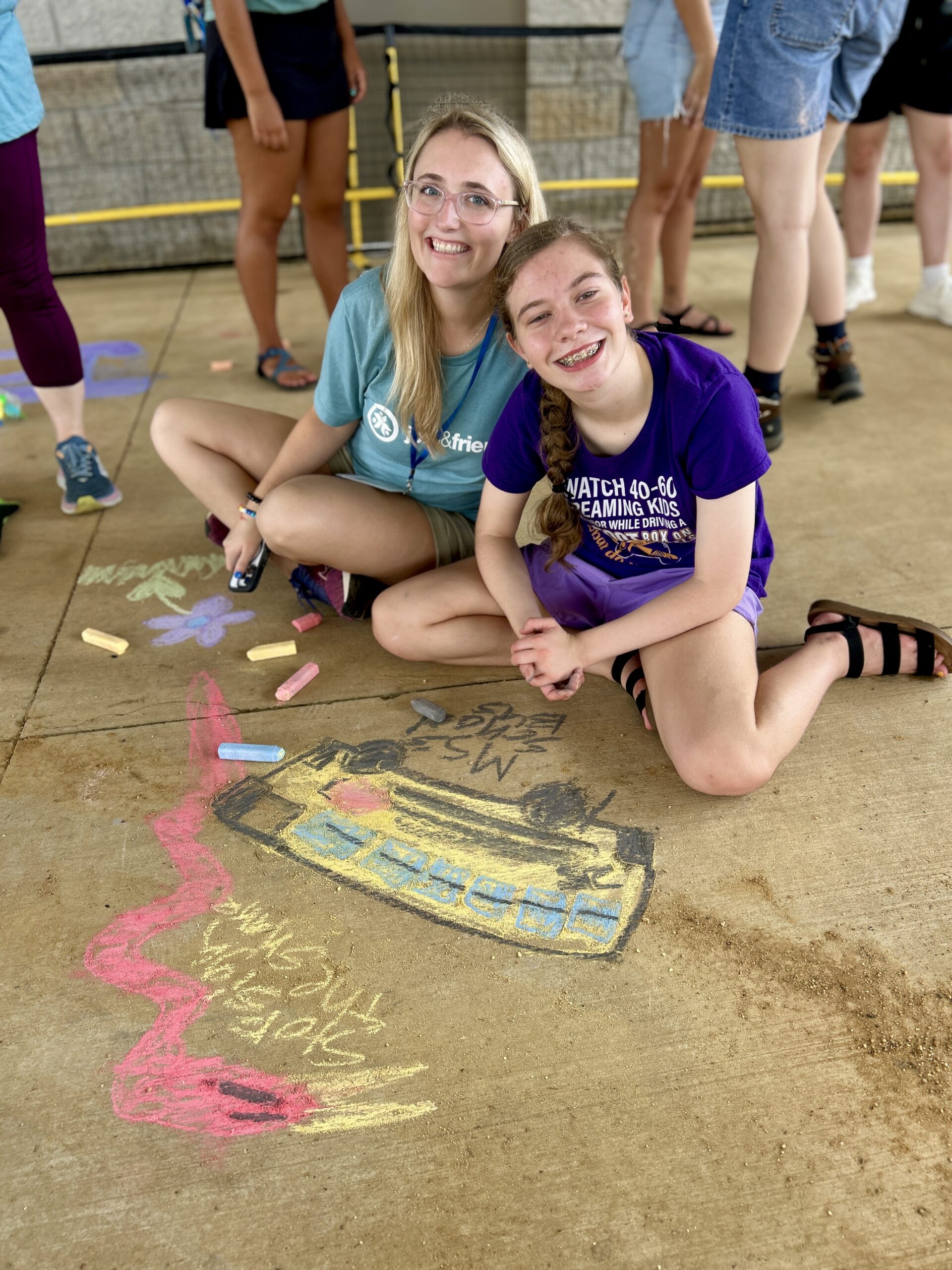 Camper and volunteer use sidewalk chalk to draw at Camp Kamassa.